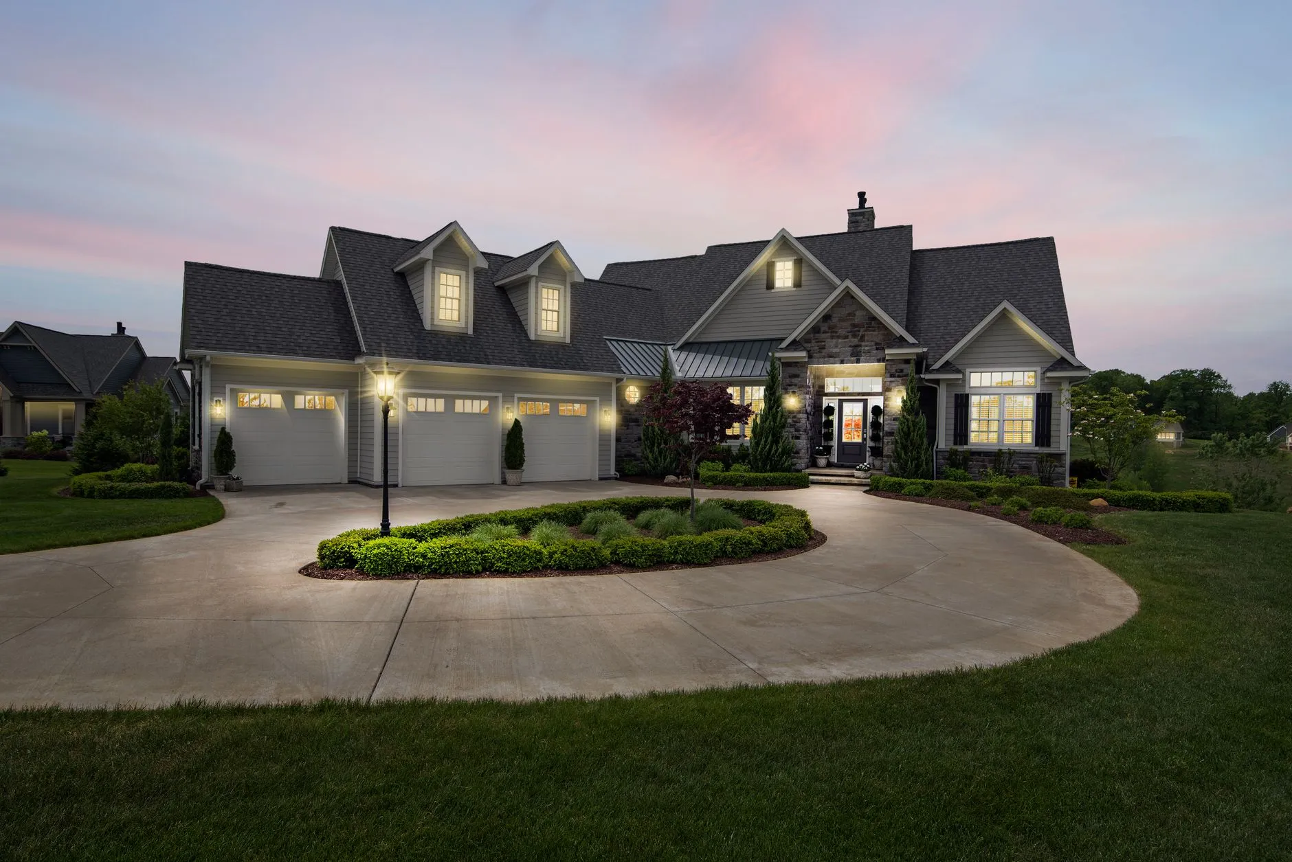 A house at dusk with path lights along the driveway, uplit trees and lit entries